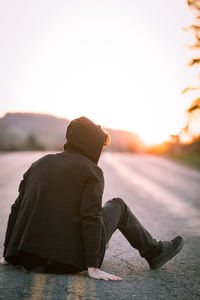 Rear view of man sitting against sky during sunset