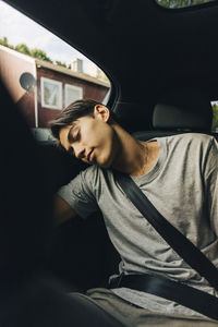 Tired young man sleeping while sitting with seat belt in car during road trip