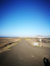 Road amidst desert against clear blue sky