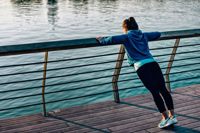 Young woman exercising on railing by river during sunset