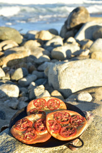 Three individual focaccia breads topped with sliced tomatoes on metal pan on rocky seashore 