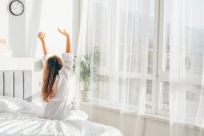 Rear view of woman sitting on bed at home