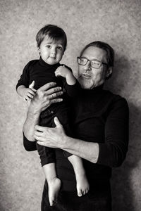 Grandfather with beard and glasses with his grandson sitting on his hands in the studio 