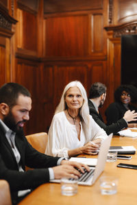 Portrait of confident businesswoman sitting by businessman using laptop at conference table in board room