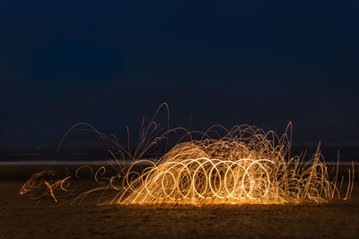 Light trails on beach against clear sky at night