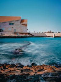 Scenic view of sea by buildings against clear blue sky