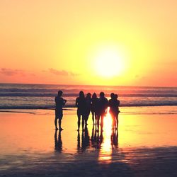 Silhouette people standing at beach against orange sky