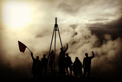 Silhouette men with arms raised against cloudy sky