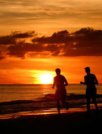 Silhouette people on beach against orange sky