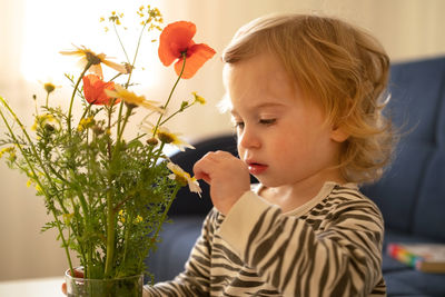 Cute girl touching flowering plant at home