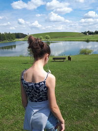 Young woman on field by lake against sky