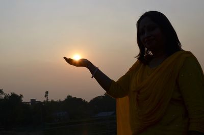 Optical illusion of woman holding sun against sky during sunset