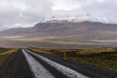 Country road leading towards mountains against sky