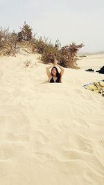 Young woman with hands clasped buried in sand