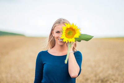 Portrait of woman holding sunflower while standing on field