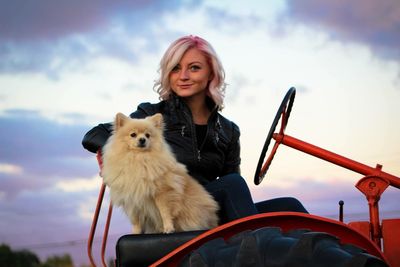 Portrait of young woman with dog against sky