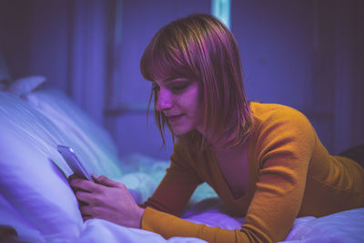 Woman using smart phone while lying on bed at home