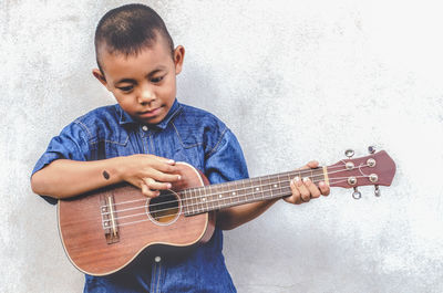 Boy playing guitar against wall