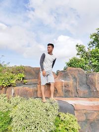 Teenage boy standing on rock formation against sky