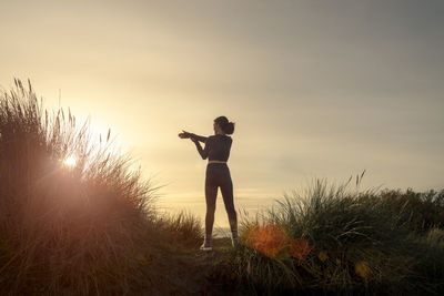 Side view of woman jumping against sky during sunset