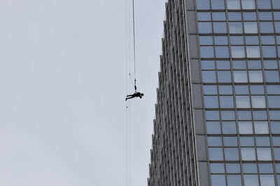 Low angle view of man hanging at crane against building
