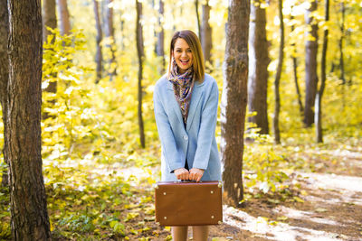 Portrait of smiling man standing by tree trunk in forest