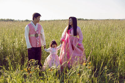 Korean family with their daughter walk in a field in the grass at sunset in summer
