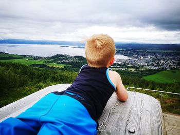 Rear view of boy lying on bench while looking at landscape