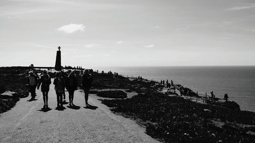 Tourists on sea coast against cloudy sky