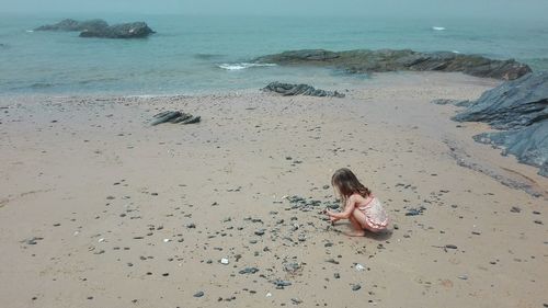 Full length of girl sitting on beach against sky