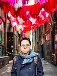 Young man standing under colorful paper decorations strung between old buildings in laneway in city.