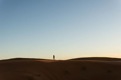 Silhouette person walking on sand dune at desert against clear sky