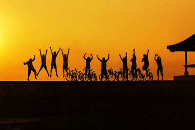 Silhouette people jumping on silhouette field against orange sky during sunset