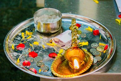 High angle view of lit diya and coins in religious plate on table