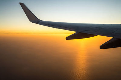 Airplane wing against sky during sunset