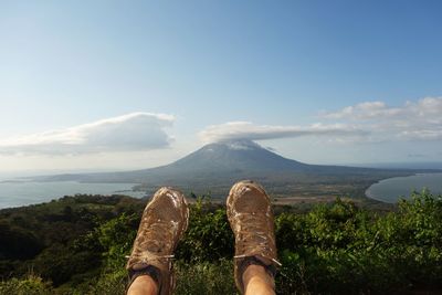 Low section of dirty shoes on mountain against sky