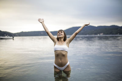 Full length of young woman with arms raised against sky