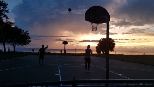 Silhouette people playing basketball against sky during sunset