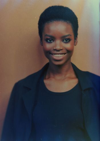 CLOSE-UP PORTRAIT OF SMILING YOUNG WOMAN STANDING AGAINST WALL