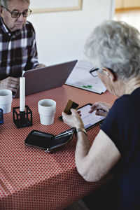 Senior woman holding credit card while using digital tablet at dining table