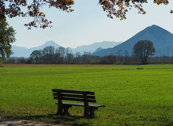 Empty bench on field by mountains against sky
