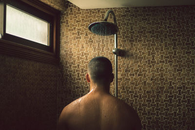 Rear view of shirtless man against wall at home
