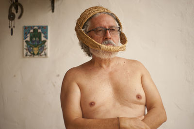 Portrait of shirtless man standing against wall at home