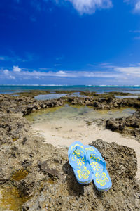 Flip-flop on rocky sea shore against sky