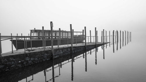 Boat moored in calm lake by wooden post against clear sky