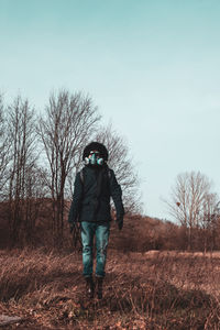 Rear view of man with mask standing on field against sky