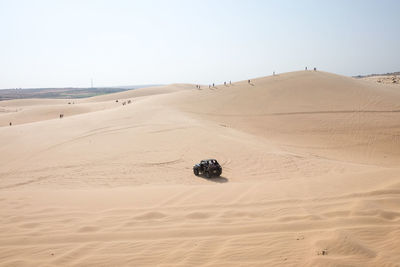 Off-road vehicle on sand at desert against clear sky