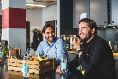 Male colleagues smiling while sitting at table in office