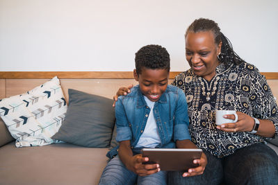 Happy boy using digital tablet while sitting with grandmother at home