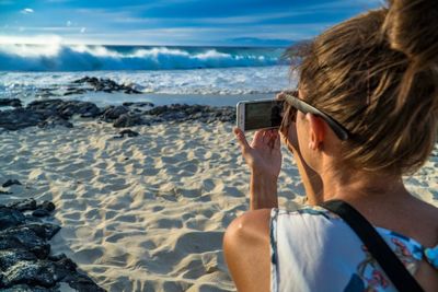 Rear view portrait of woman photographing beach